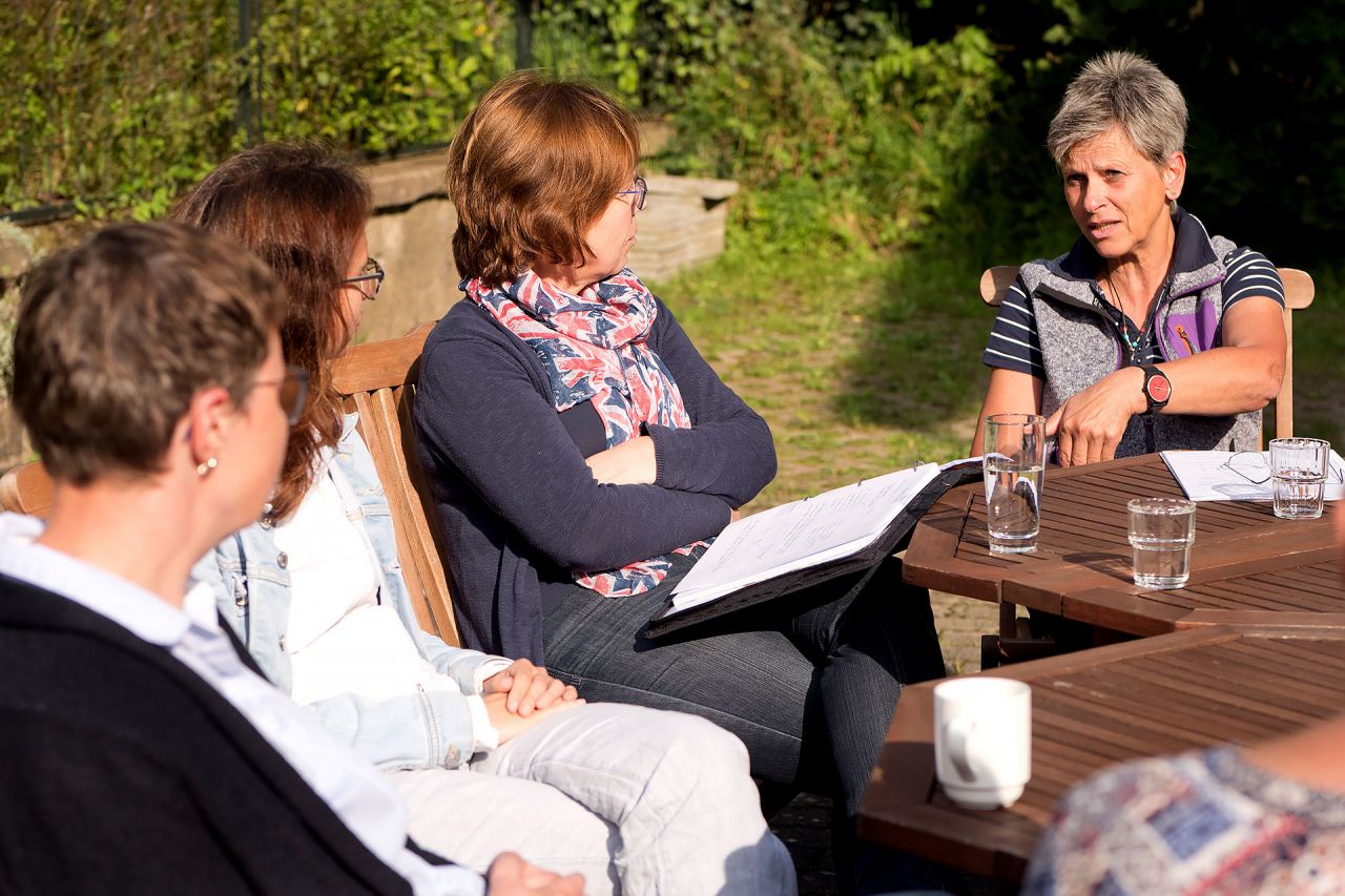 Teilnehmende der Ausbildung «Individualpsychologischer Berater ADI®» diskutieren draussen an einem Tisch in der Sonne