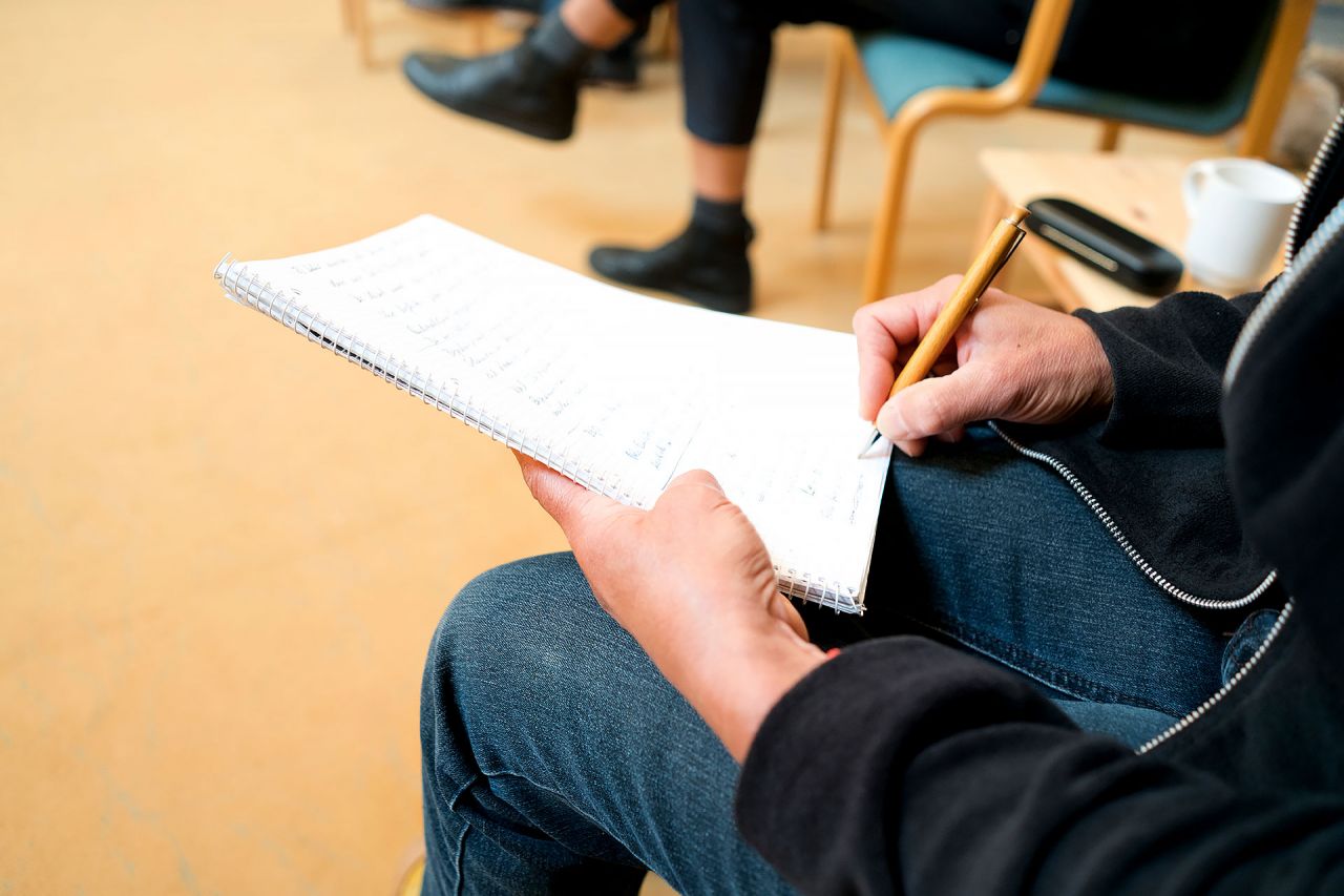So lernen Sie in der Ausbildung «Individualpsychologischer Berater ADI®» Leute im Sitzkreis, Hand mit Stift notiert fleissig mit