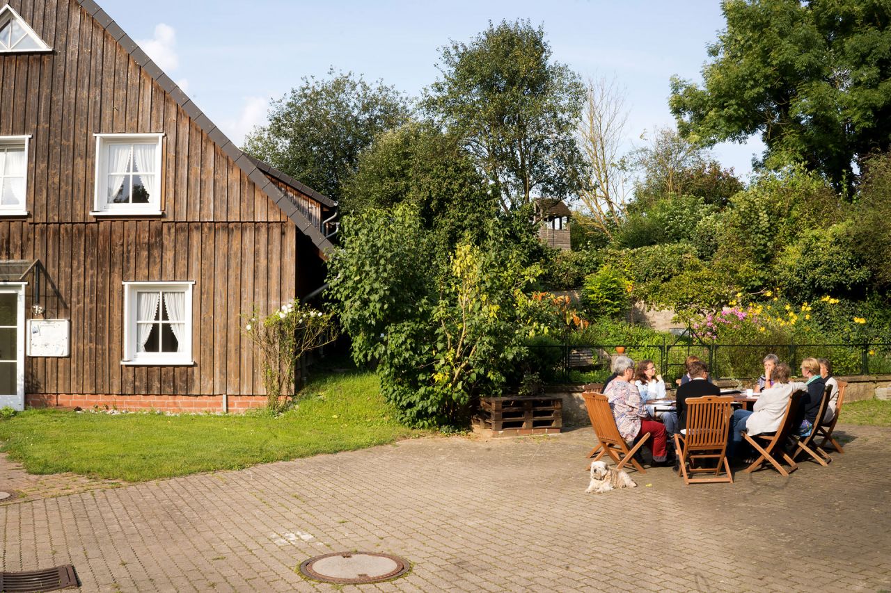 Eine Gruppe Teilnehmende sitzt an der Sonne auf dem Platz in der alten Mühle