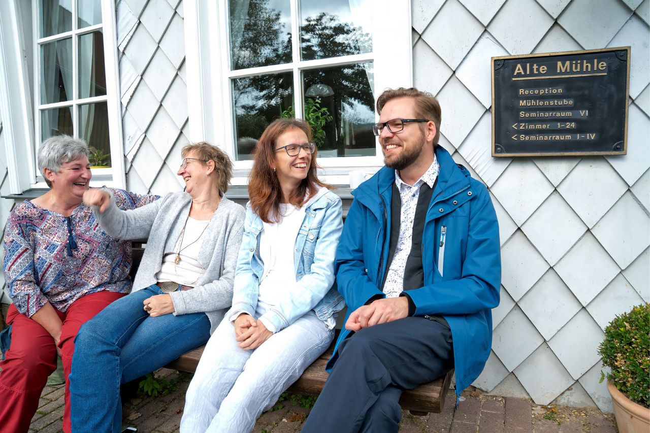 Seminarteilnehmende sitzen lachend auf einer Bank in der Sonne