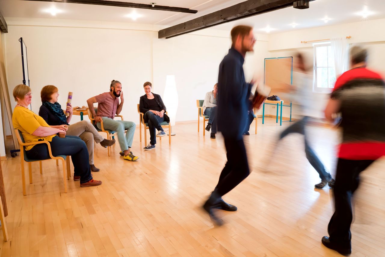 Selbsterfahrung steht im Mittelpunkt des Individualpsychologischen Intensivseminares Leute mit Instrumenten in der Hand bewegen sich im Kreis und tanzen